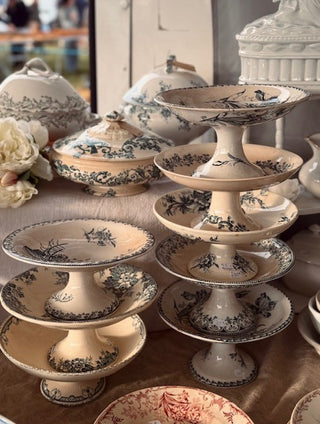 A collection of vintage ceramic serving pieces, including tiered cake stands, lidded sugar bowls, and plates, decorated with a classic blue and cream toile pattern.