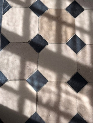 Beige and black geometric floor tiles with a repeating diamond pattern, shown in natural light with soft shadows.